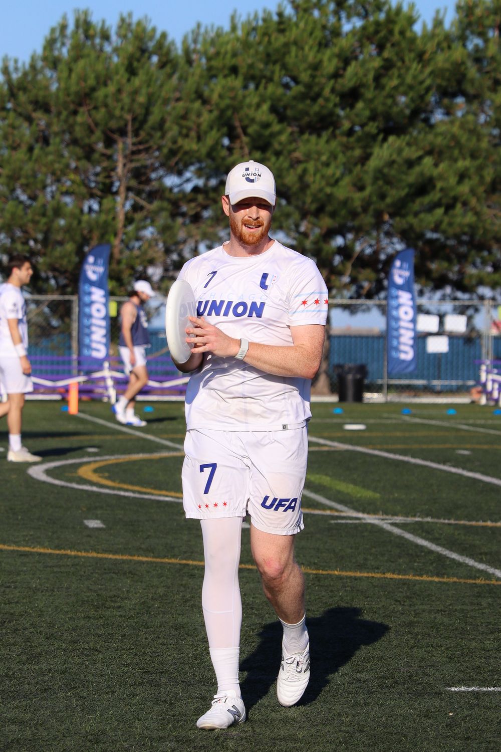 Ultimate frisbee player in white uniform warming up on athletic field during daytime match.