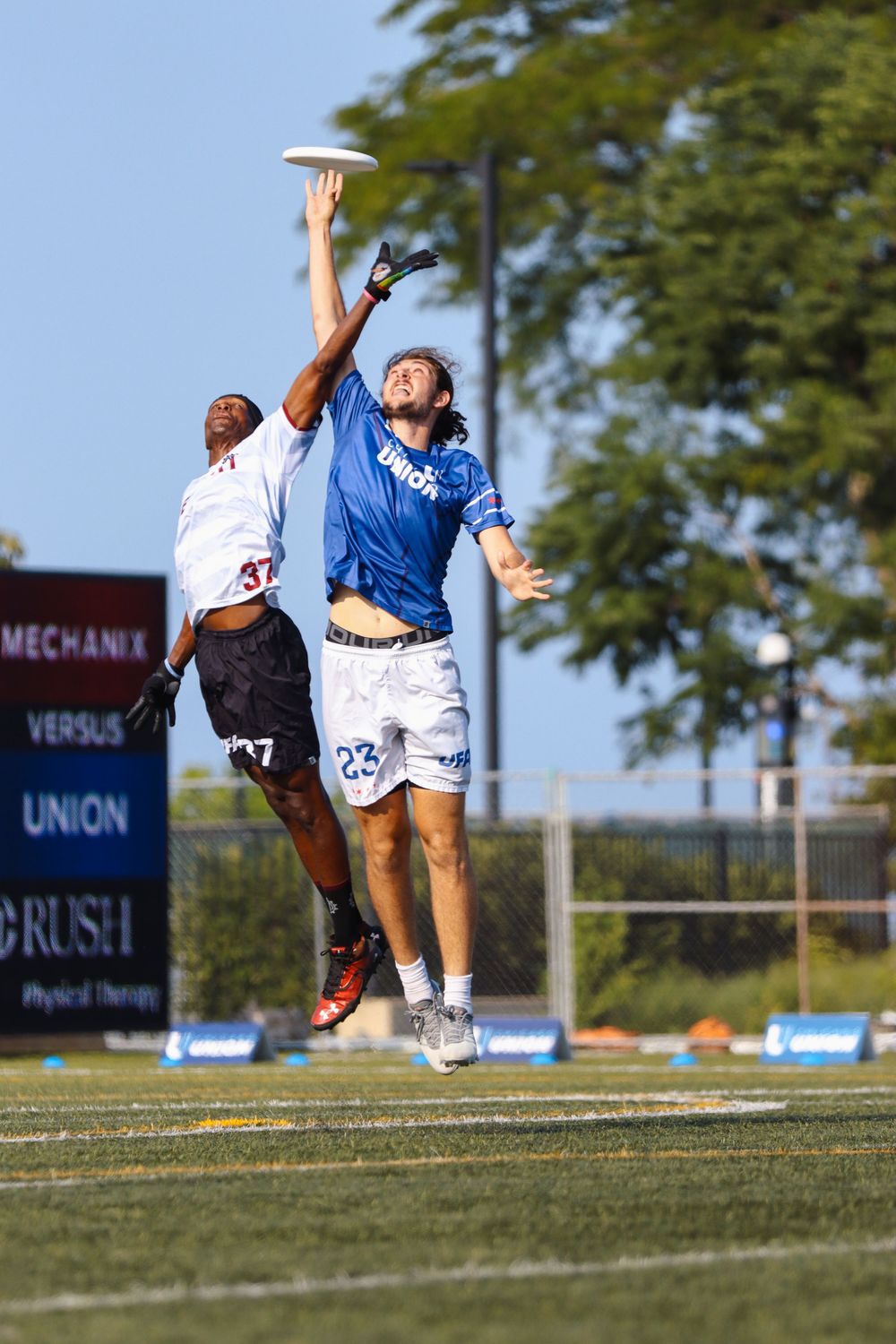 Players leaping high to catch frisbee during competitive ultimate match on grass field.