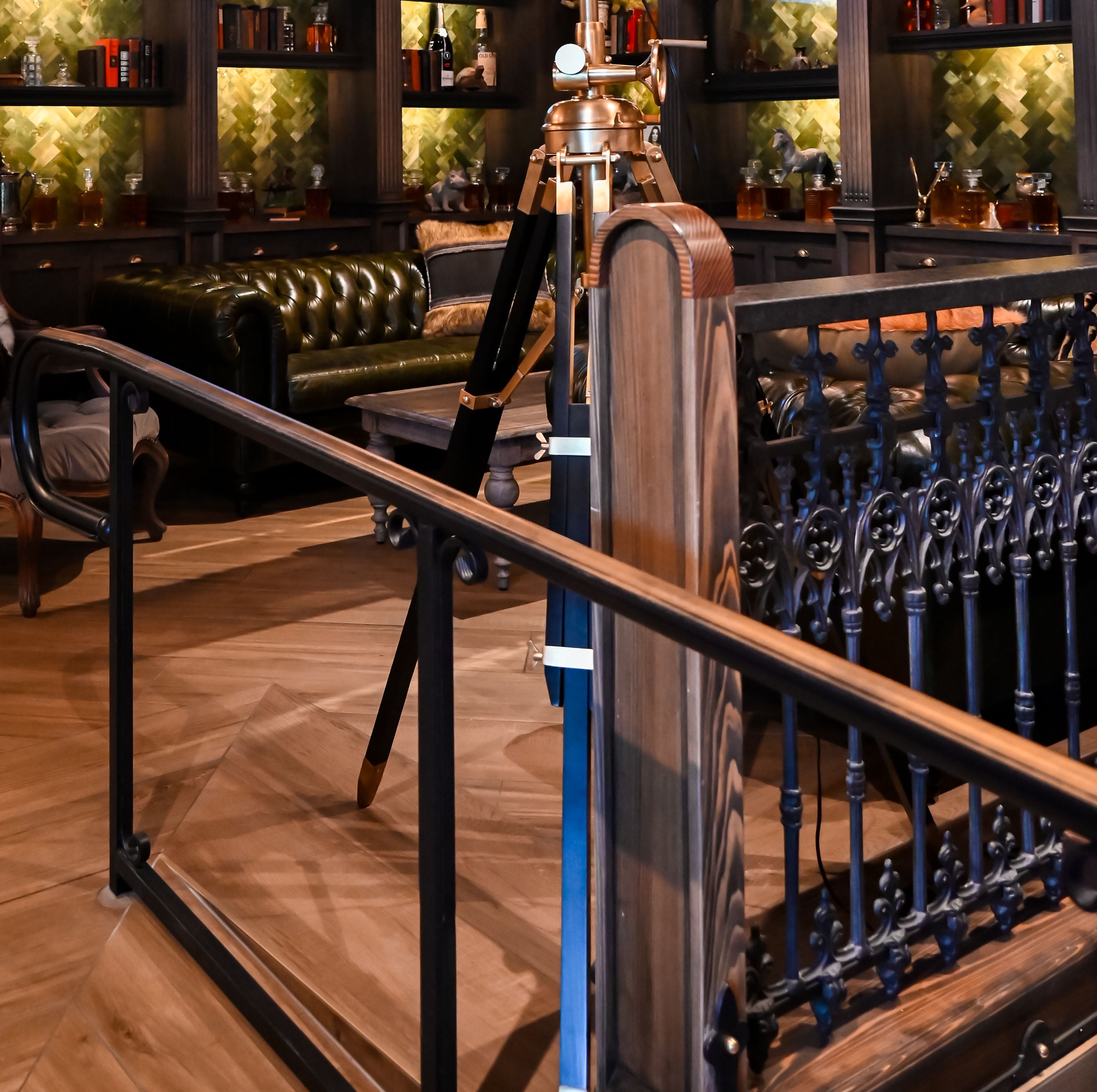Elegant bar interior with ornate iron railings and illuminated bottle displays.