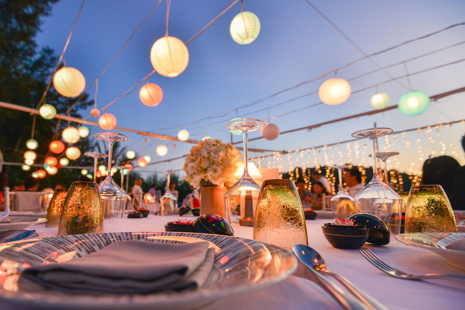 Outdoor dinner table setting with string lights creating a romantic atmosphere at dusk.