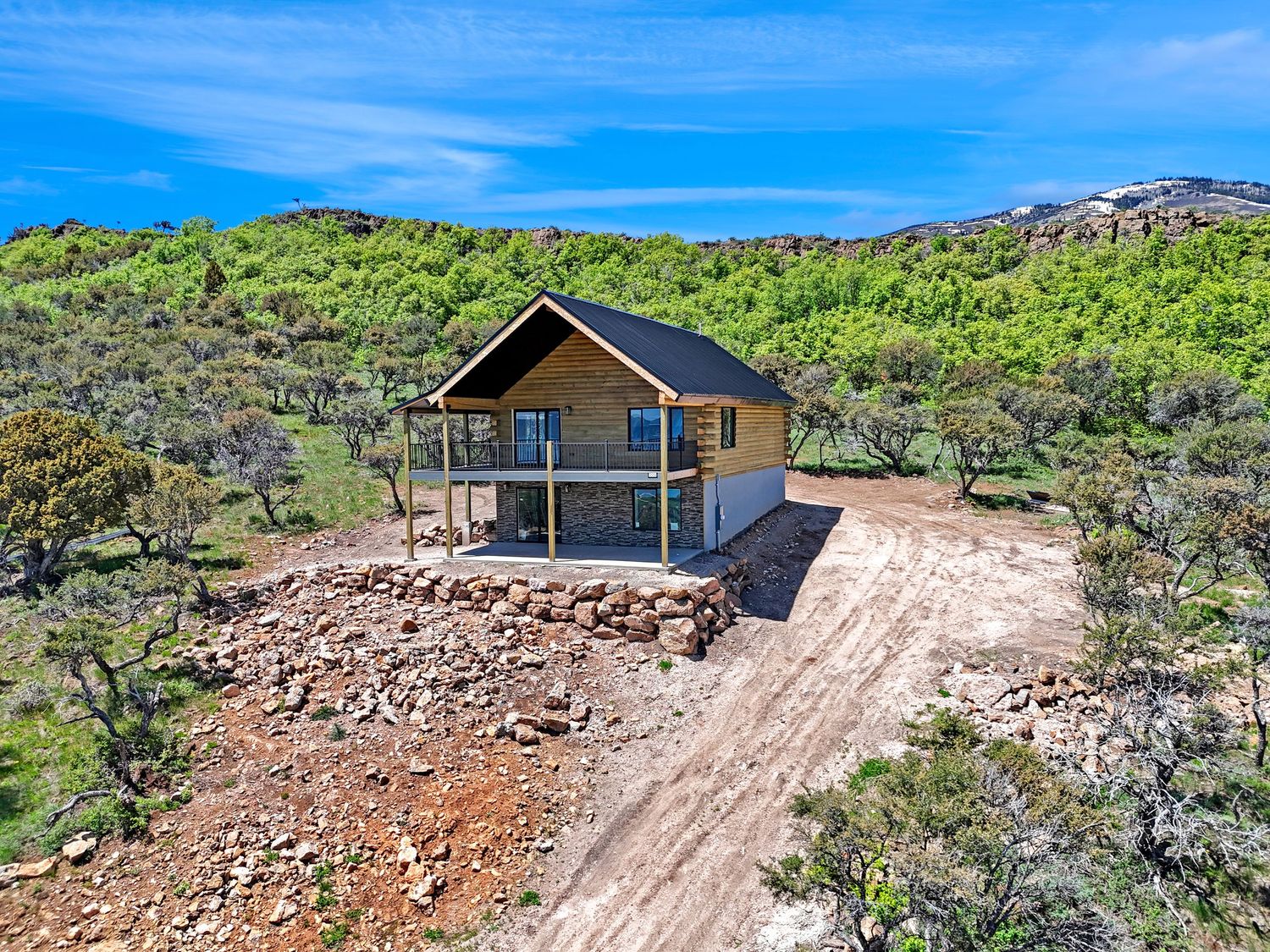Aerial view of a modern cabin nestled on a rocky hillside surrounded by lush green shrubs and trees.
