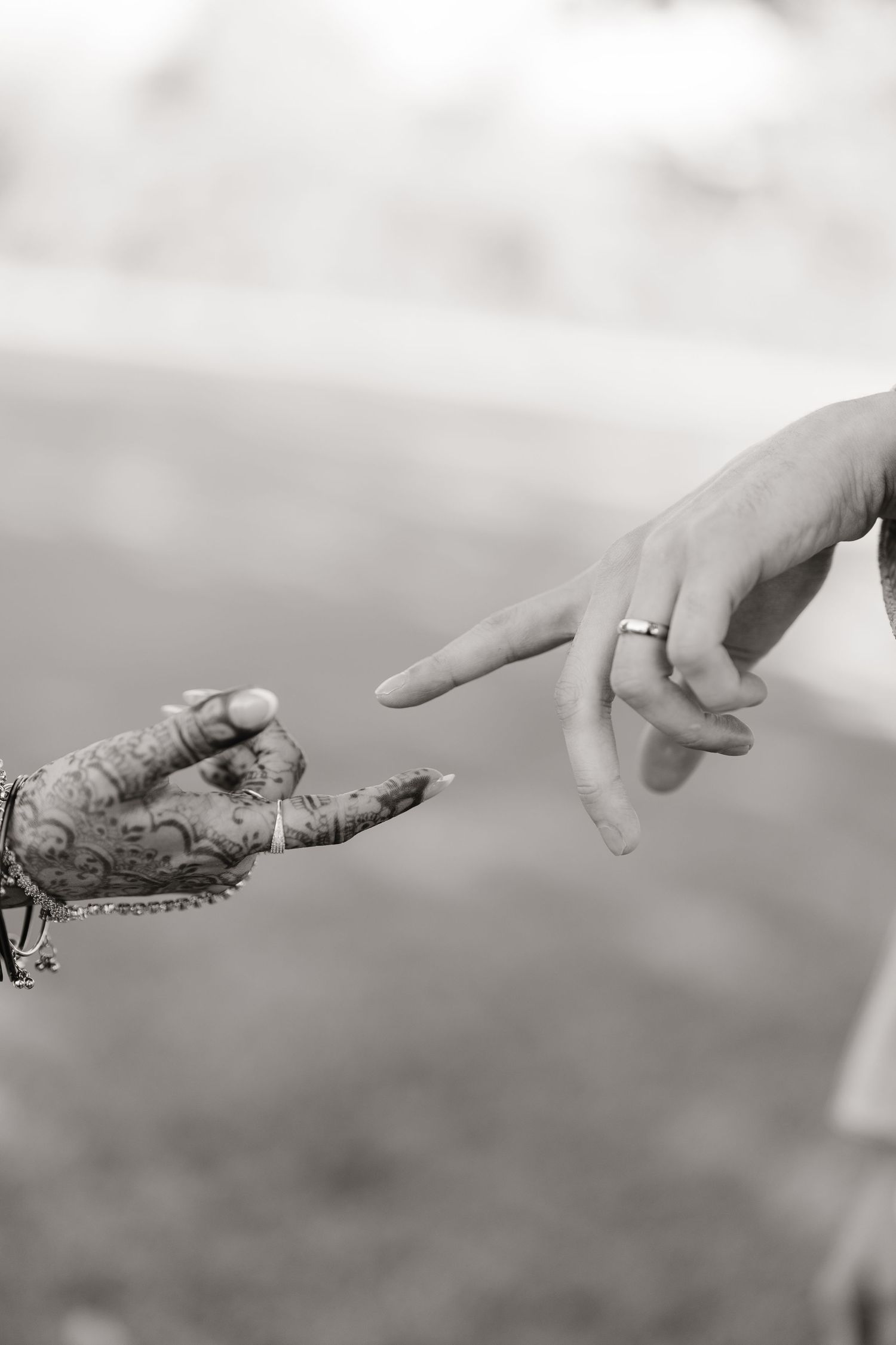 Black and white close-up of South Asian bride and groom hands with henna, bangles, and wedding rings.