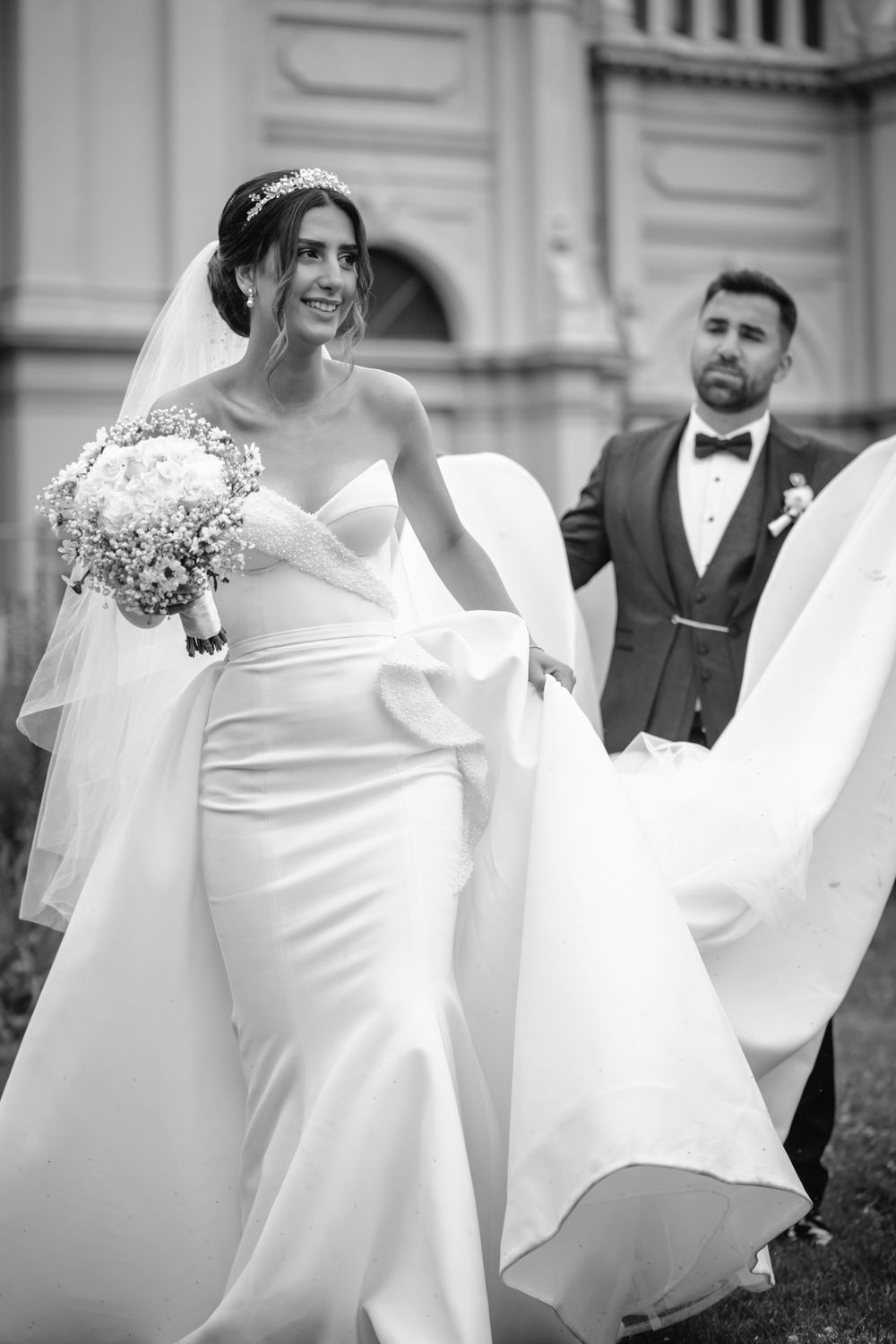Black and white photo of a bride in a fitted wedding dress with flowing train outdoors.