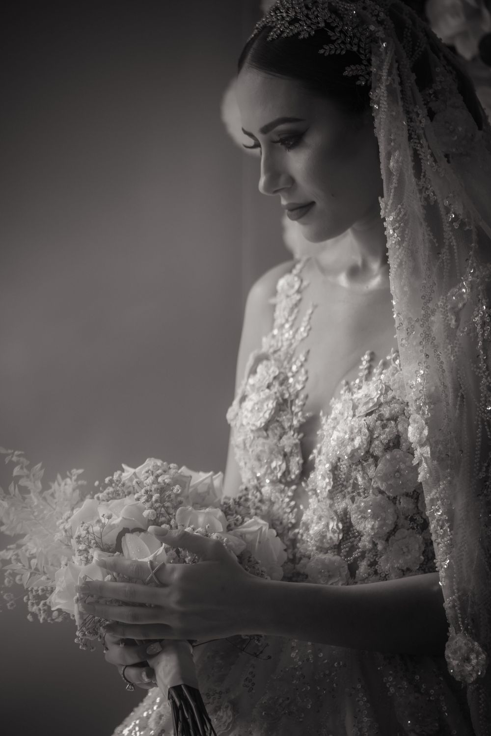 Black and white portrait of a bride holding a bouquet in an elegant lace wedding dress and veil.