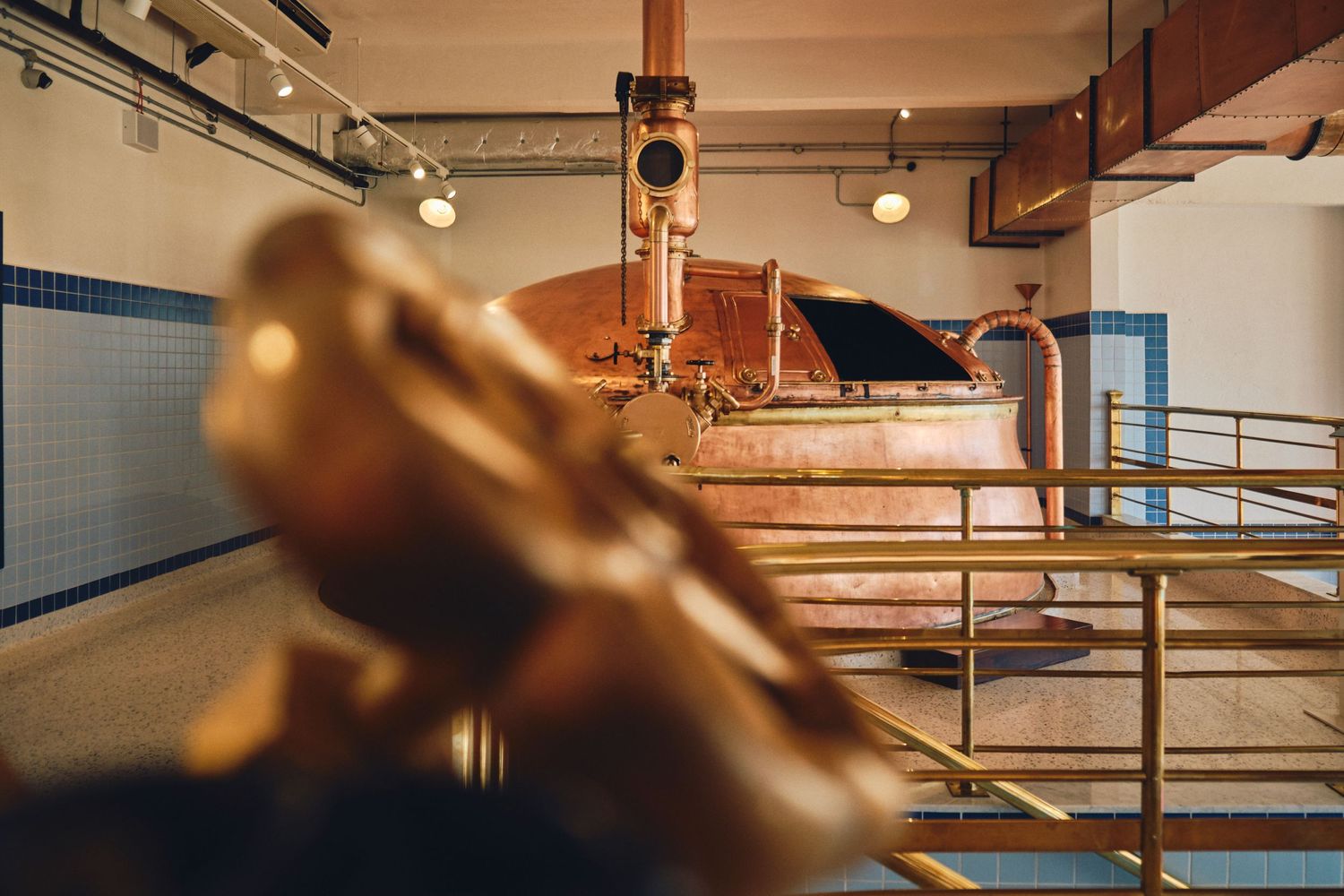 Interior view of a brewery showing copper brewing equipment and metal railings.