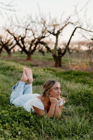 Someone wearing a light blue dress lies on grassy ground in an orchard during springtime.