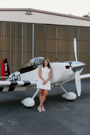 Small white private aircraft parked in front of an aviation hangar with fall foliage visible in background.
