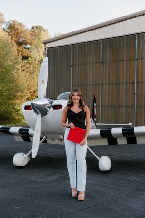 A small private aircraft parked on a tarmac near a hangar with fall foliage in the background.