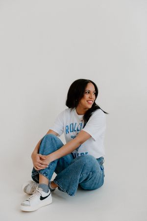 Woman wearing casual white t-shirt and jeans sits on floor against white background posing in Nike sneakers.