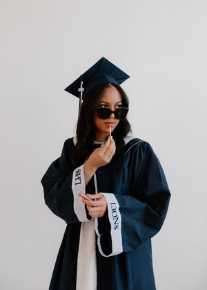 Graduate in cap and gown poses against white backdrop in series of celebratory shots during graduation photoshoot.