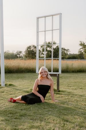 A figure lies on green grass with artistically arranged white window frames creating a dreamy outdoor scene.