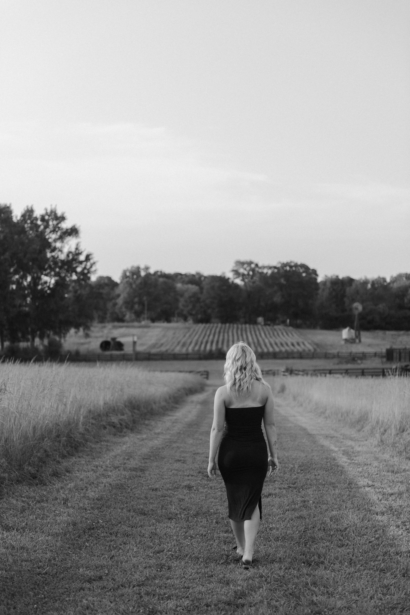 A black and white photo series shows someone walking through a serene rural field path.