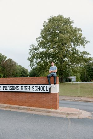 Someone sits atop a brick wall entrance sign for Persons High School on a sunny day.