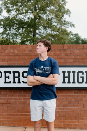 Student stands confidently against a brick wall with 'High' lettering wearing a navy t-shirt and white shorts.