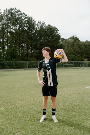An athlete practices throwing techniques with a volleyball on a grassy sports field.