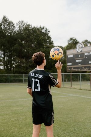 Soccer player in a Bulldogs jersey number 13 performs ball tricks on an athletic field with scoreboard in background.