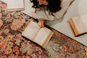 Overhead view of person reading books while lying on ornate floral patterned area rug.