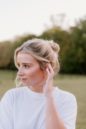 Profile view sequence of person in white shirt brushing blonde hair behind ear outdoors.