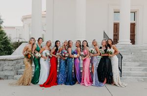 Group of people wearing colorful formal attire sitting on white stone steps for a celebratory photograph.