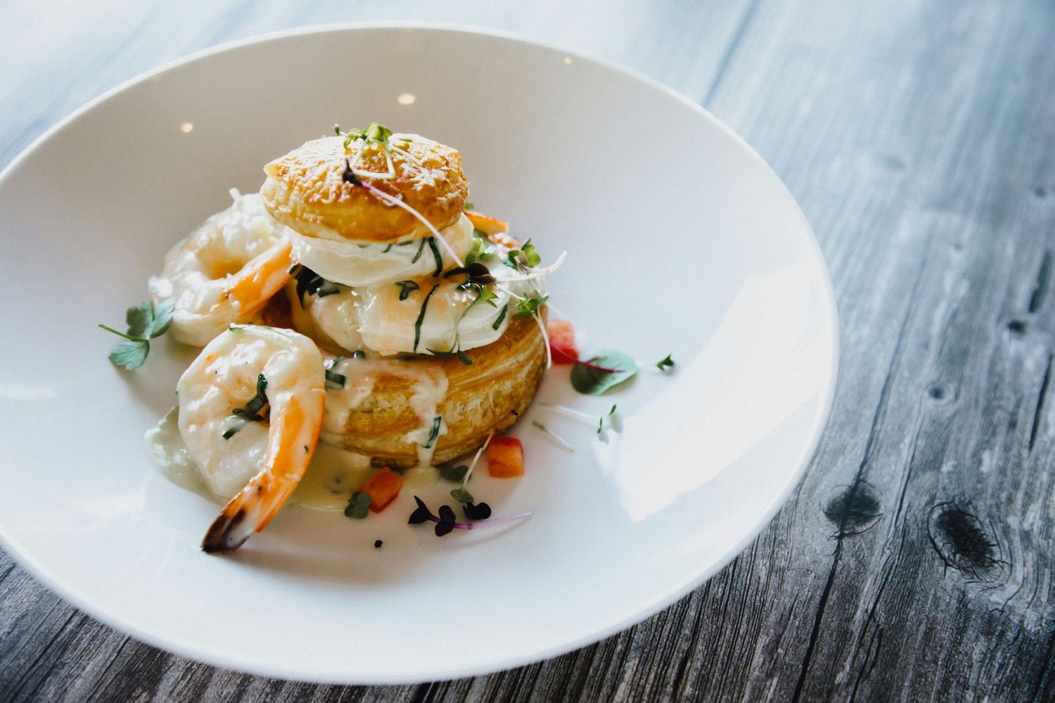 Elegant seafood dish featuring grilled shrimp and sauce on a round white plate against rustic wooden surface.