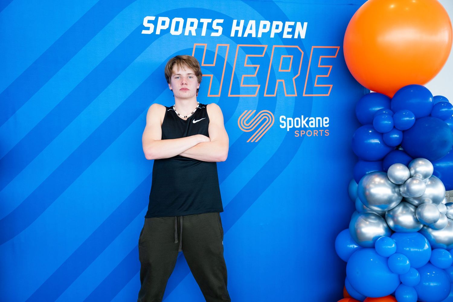 Athlete posing against blue wall with 'Sports Happen Here' text and balloon decorations.