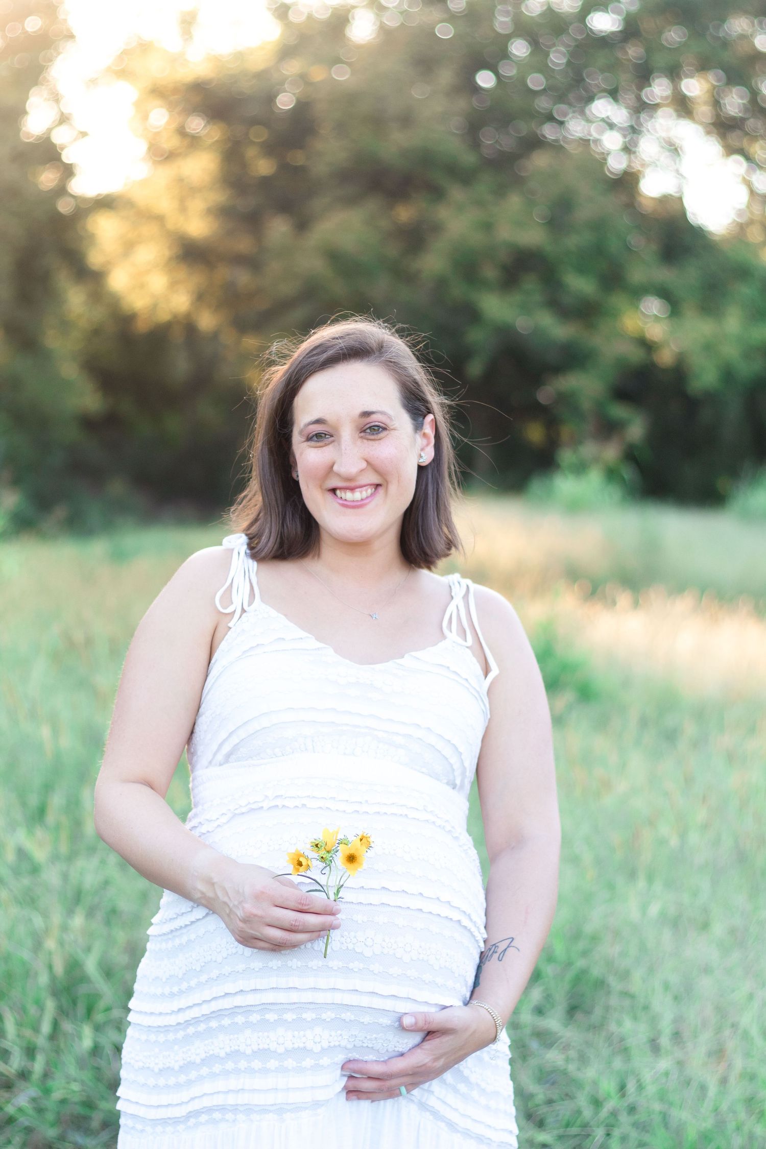 Pregnant mother smiling at camera with sun coming in behind her.