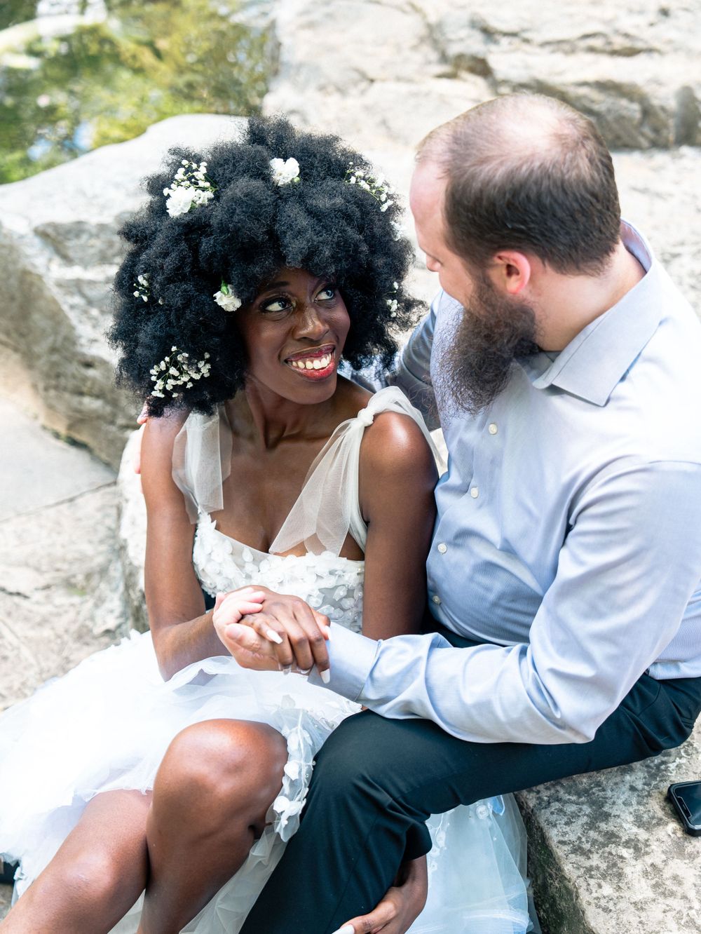 Couple sitting on rocks sharing intimate moment with flowers in hair.