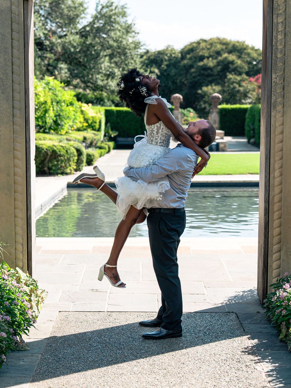A playful lift pose in a garden archway with a reflecting pool in the background.