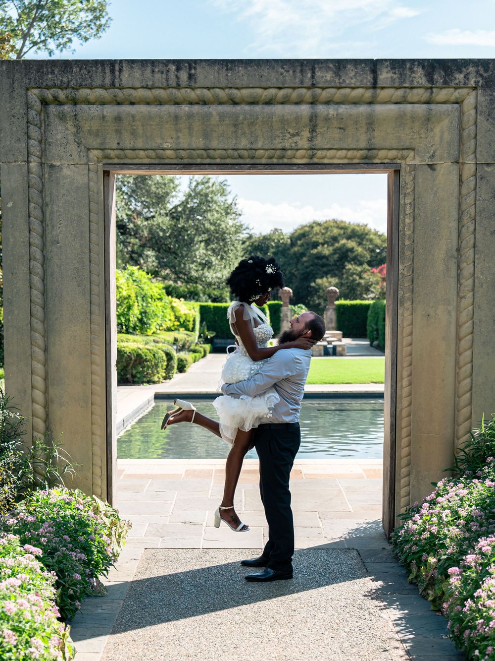 A romantic lifting pose framed by a stone archway with a garden pool setting.