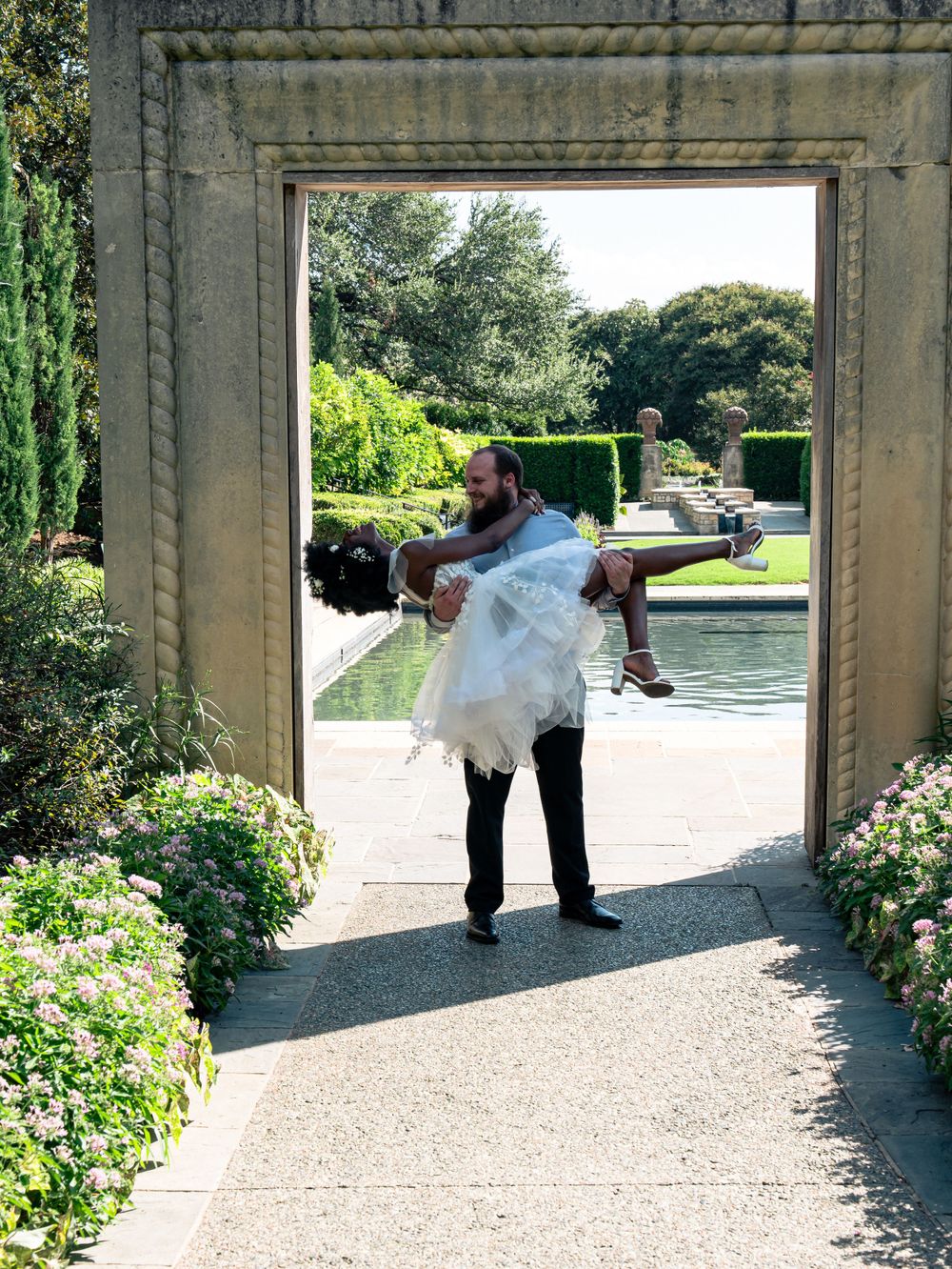 A couple in an intimate dance pose through a stone garden archway with a pool view.