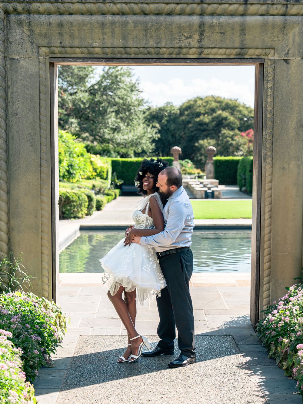 A loving embrace in a stone archway with a formal garden and pool in the background.