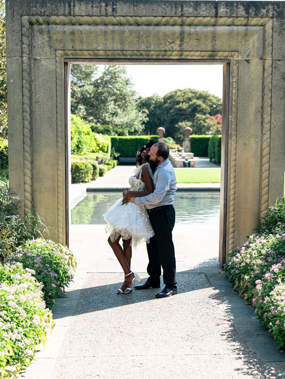 A romantic dance pose framed by a stone archway with flowering gardens.