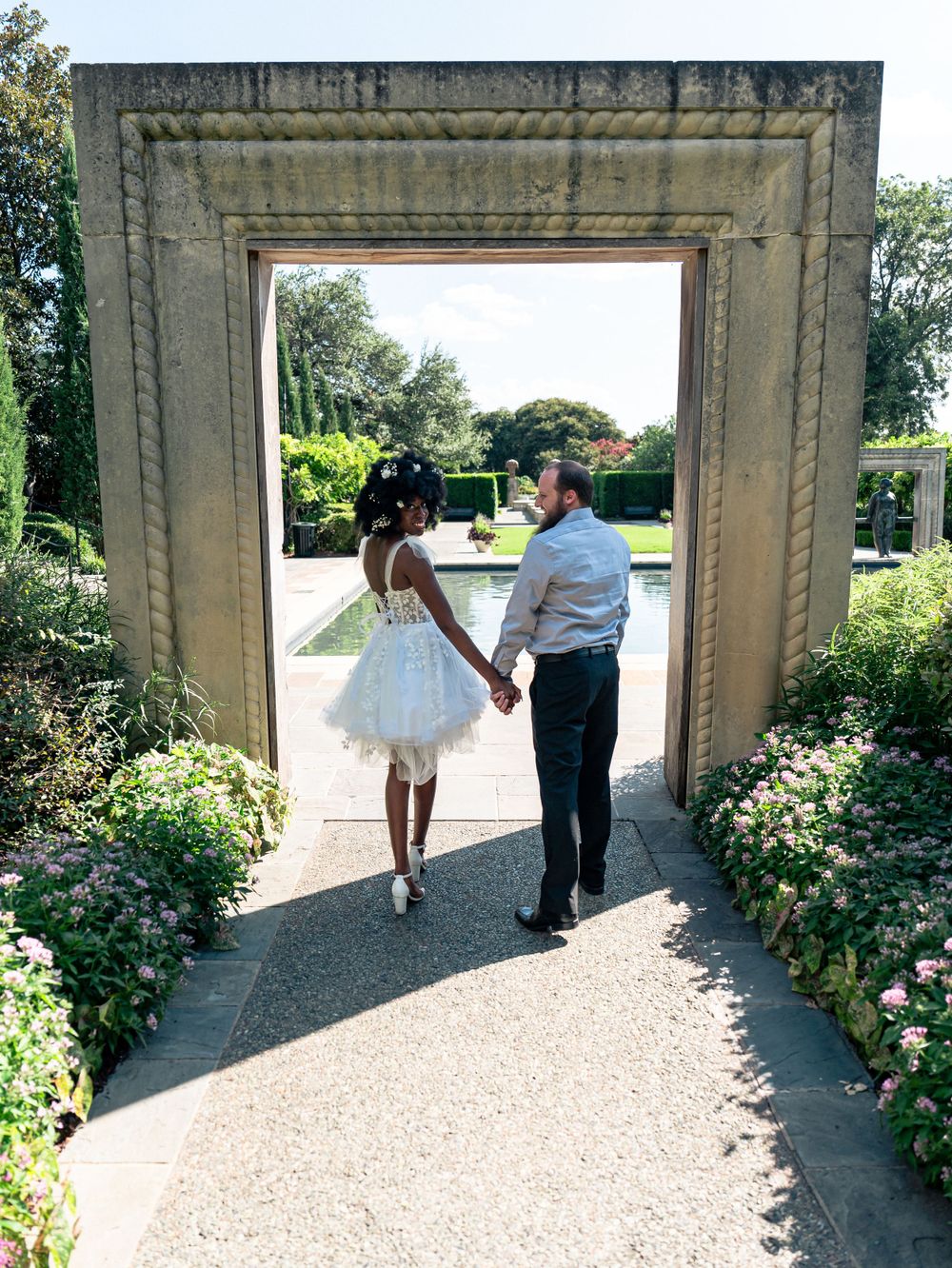 A couple walking hand in hand through a stone archway in a formal garden setting.