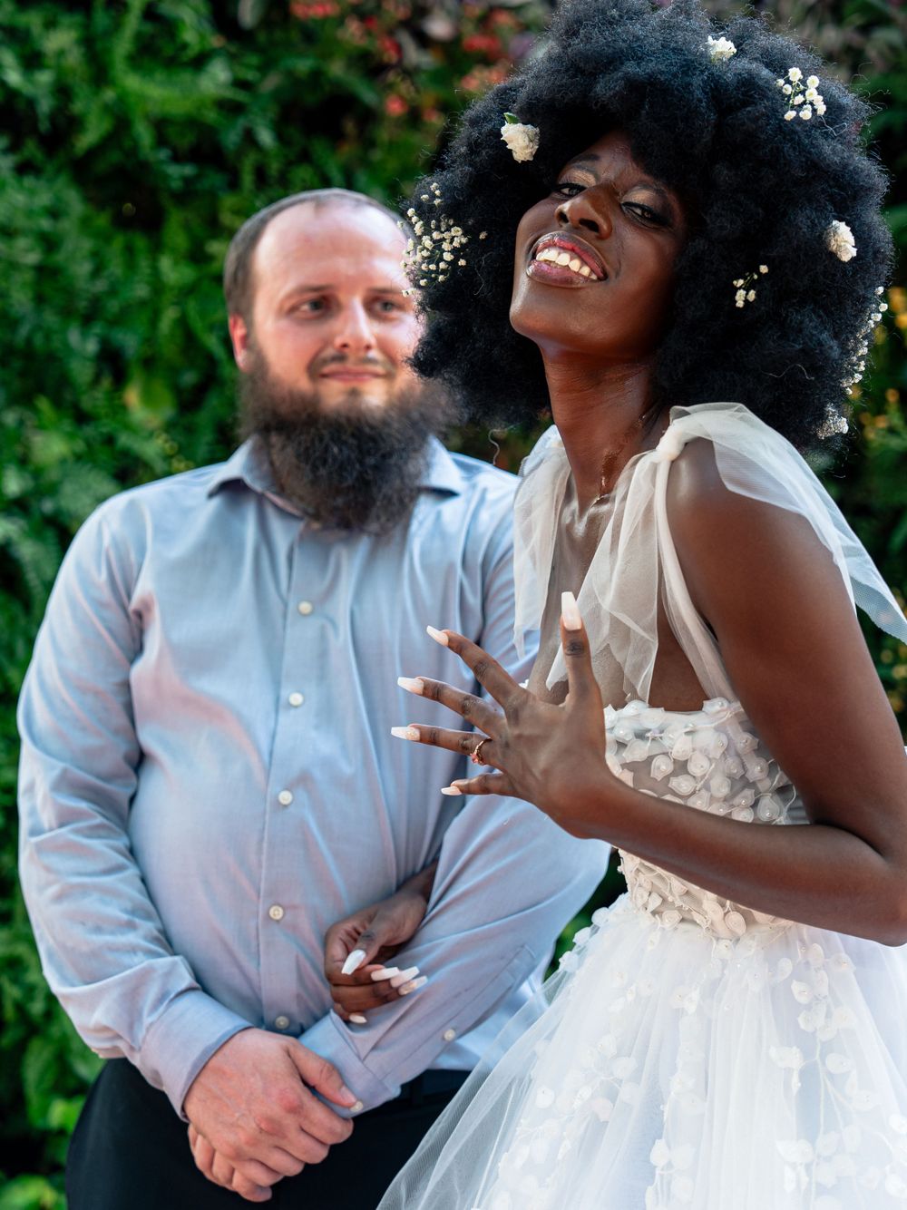 A beautiful wedding couple shares a joyful candid moment in a garden setting with flowers in the bride's natural hair.