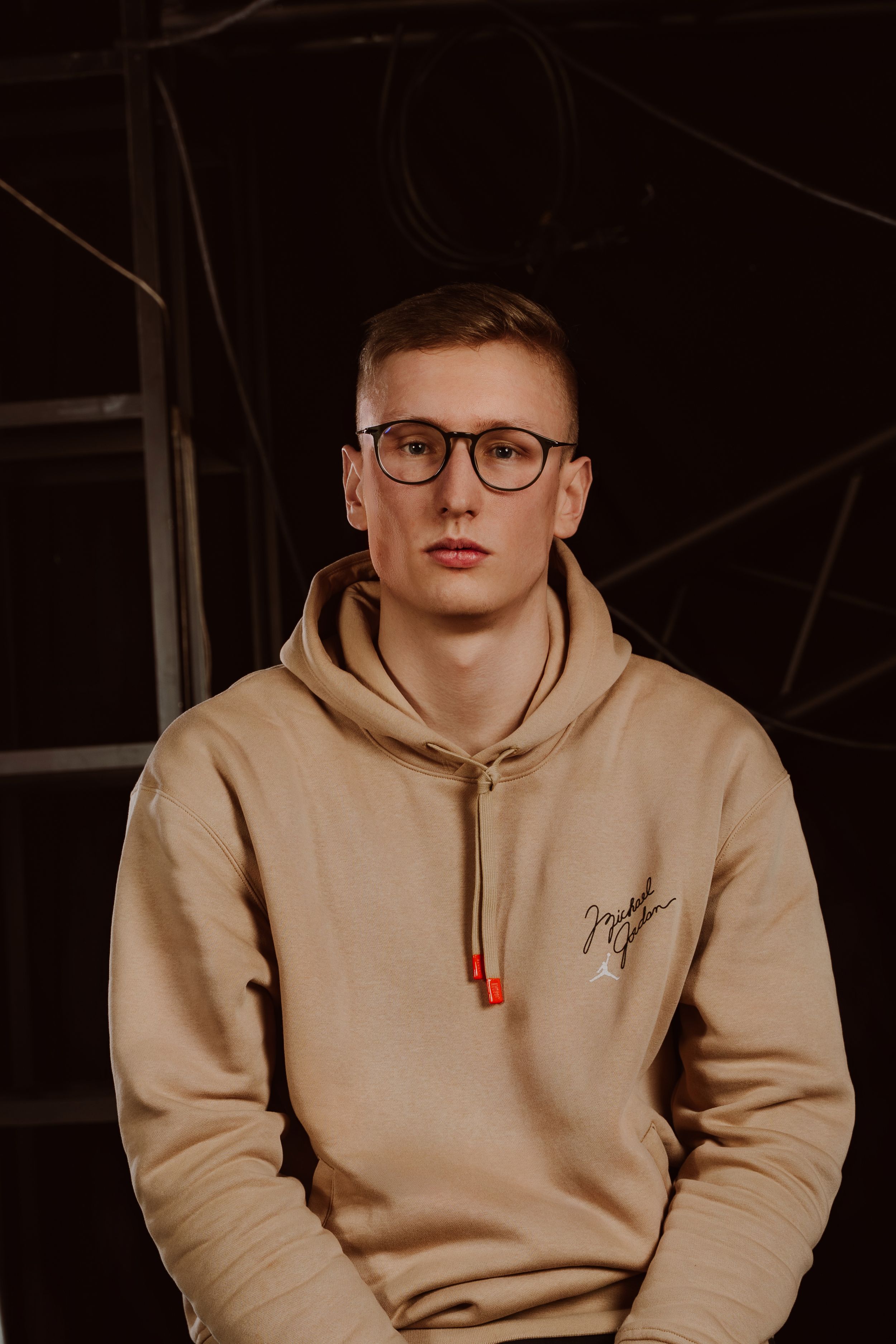 Fashion portrait of a person in a beige/tan sweater against a dark background