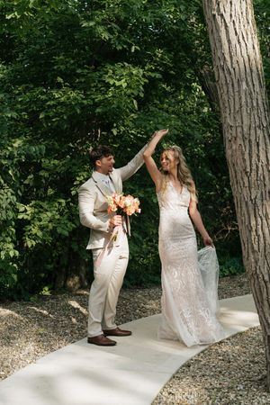 A couple celebrates their wedding day outdoors in a natural setting with a white walkway and lush greenery.