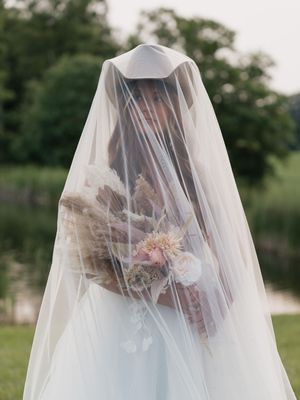 Romantic portrait with bride under sheer veil in front of lush green outdoor garden setting.