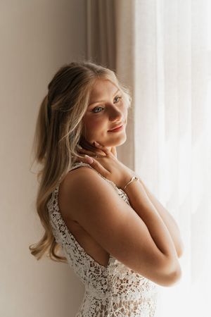 Side view sequence of woman in white lace dress with blonde hair posing against bright window.