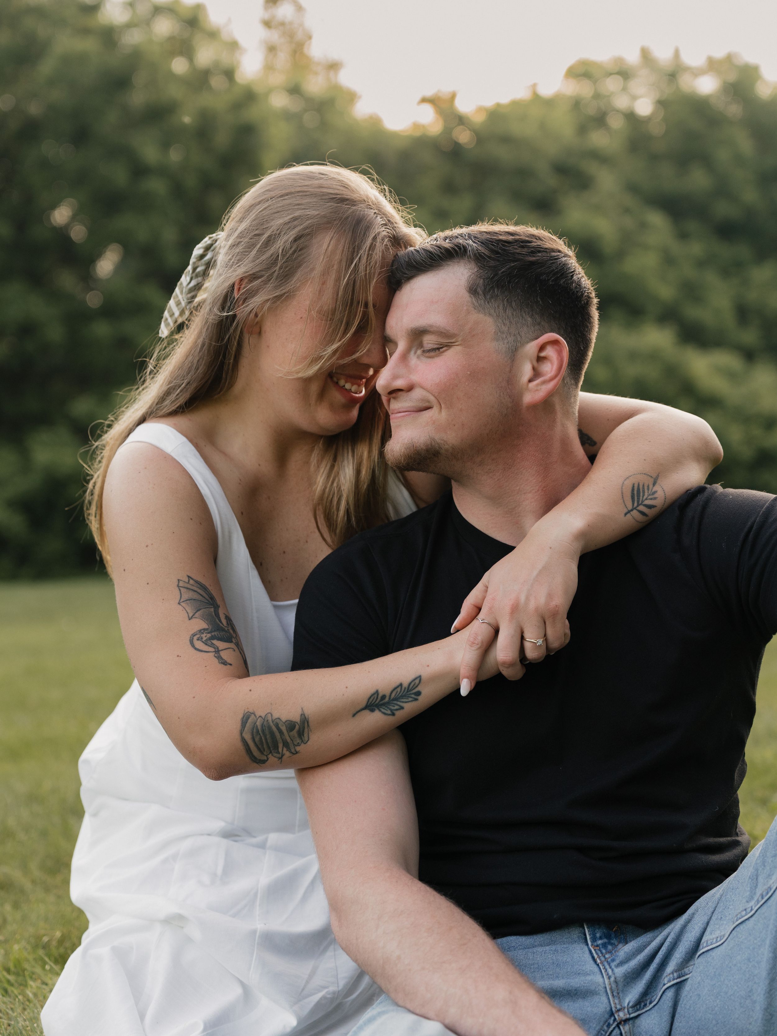 A romantic couple shares tender moments while sitting outdoors in a park during golden hour.