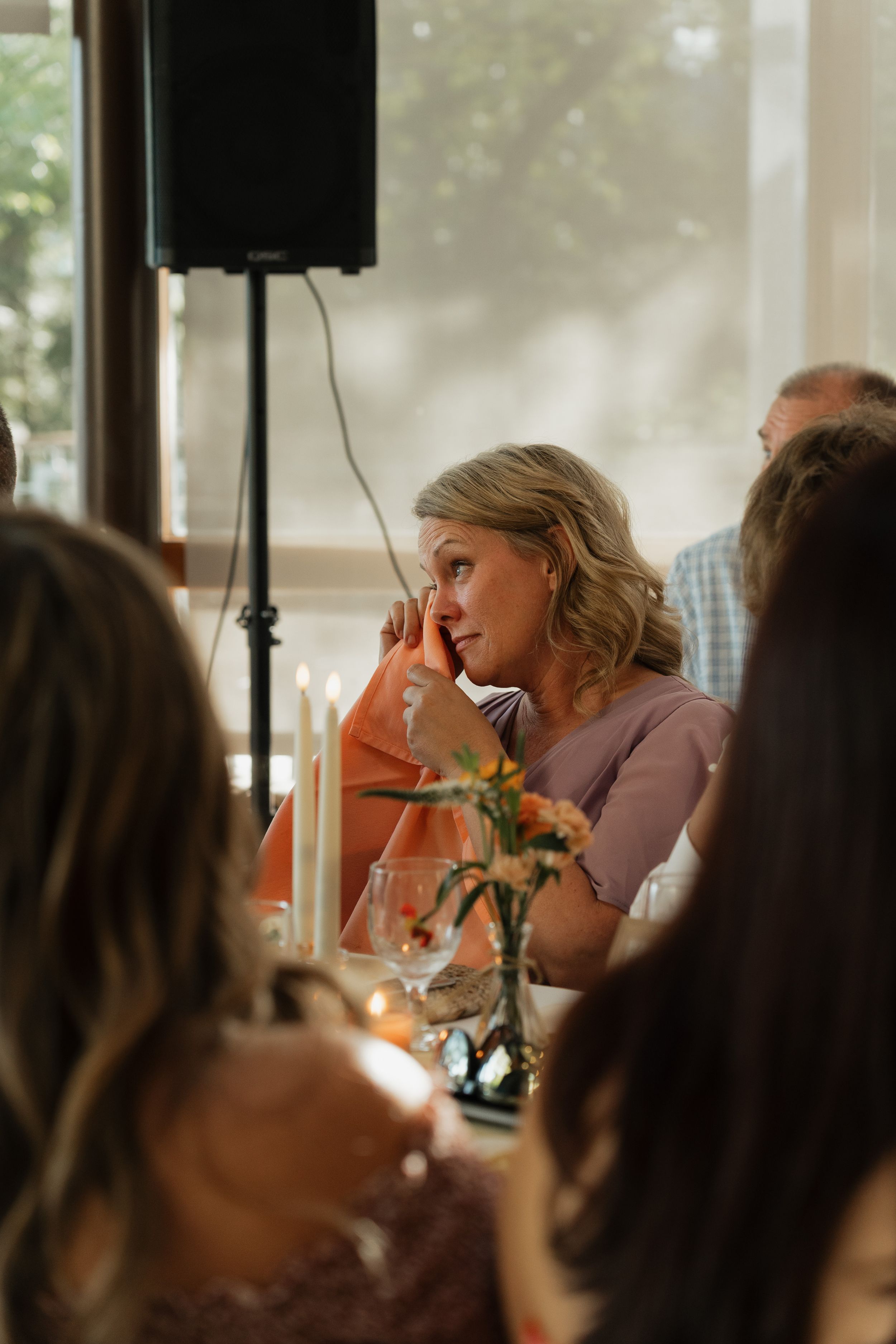 Guests gather around a dining table with flowers in soft natural light through windows.
