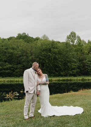 A newly married couple shares a joyful moment in a scenic green meadow with forest backdrop during their wedding celebration.