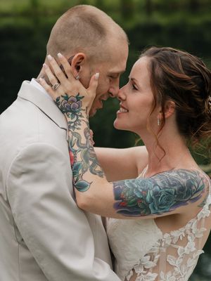 A romantic wedding portrait showing a couple in white embracing, with visible colorful tattoos on both their arms.