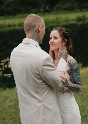 A couple in wedding attire share an intimate dance together outdoors with a lake and trees in the background.