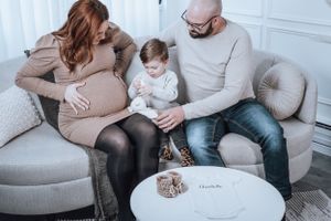 Expecting parents and child sharing intimate moment on grey couch.