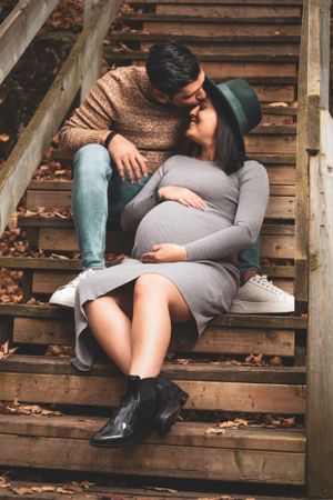 Intimate maternity portrait on wooden stairs surrounded by fallen autumn leaves.