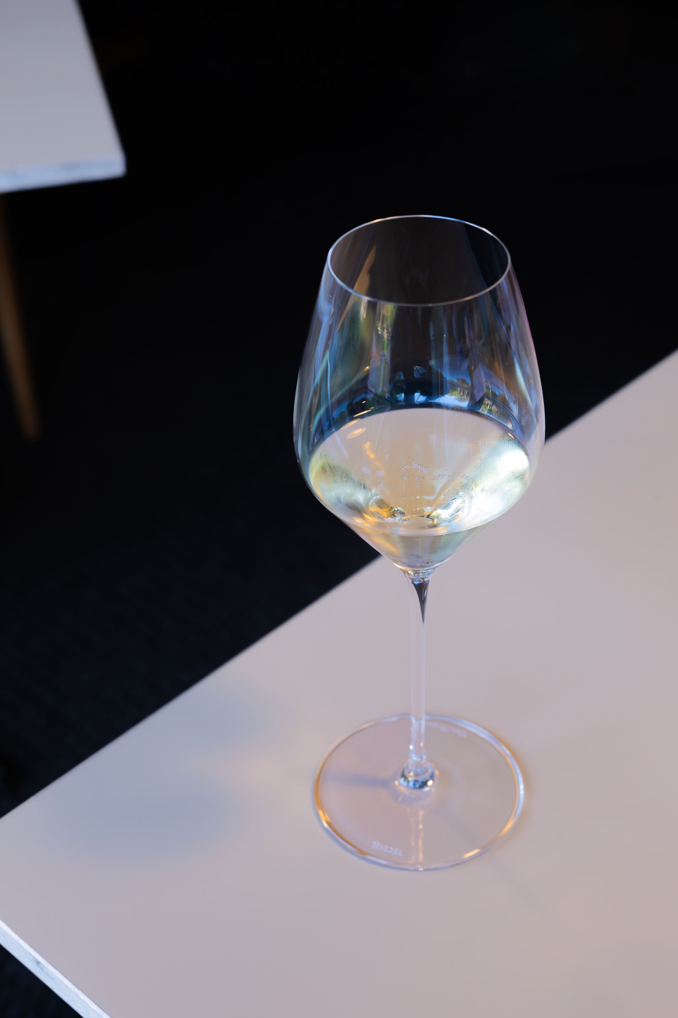 A glass of white wine on a white surface against a dark background.