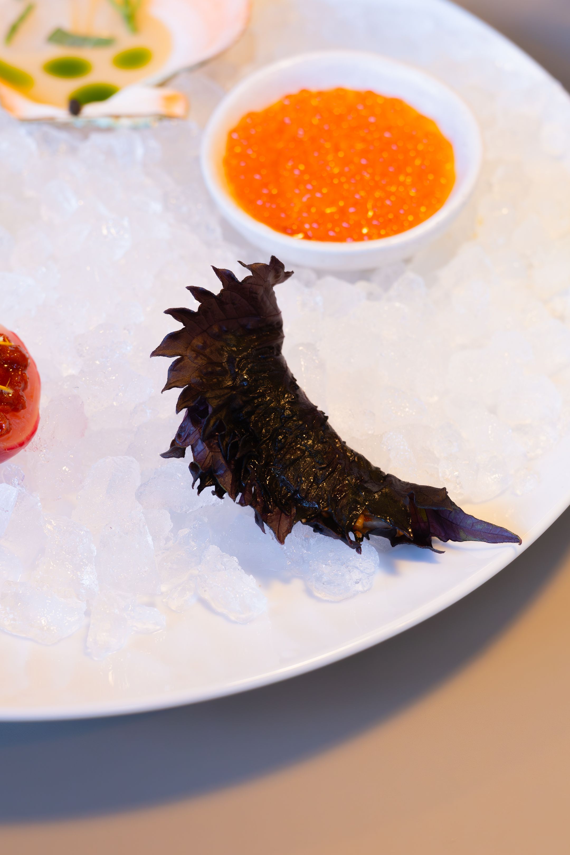 Sea cucumber and caviar sauce presented on a white plate with crushed ice.