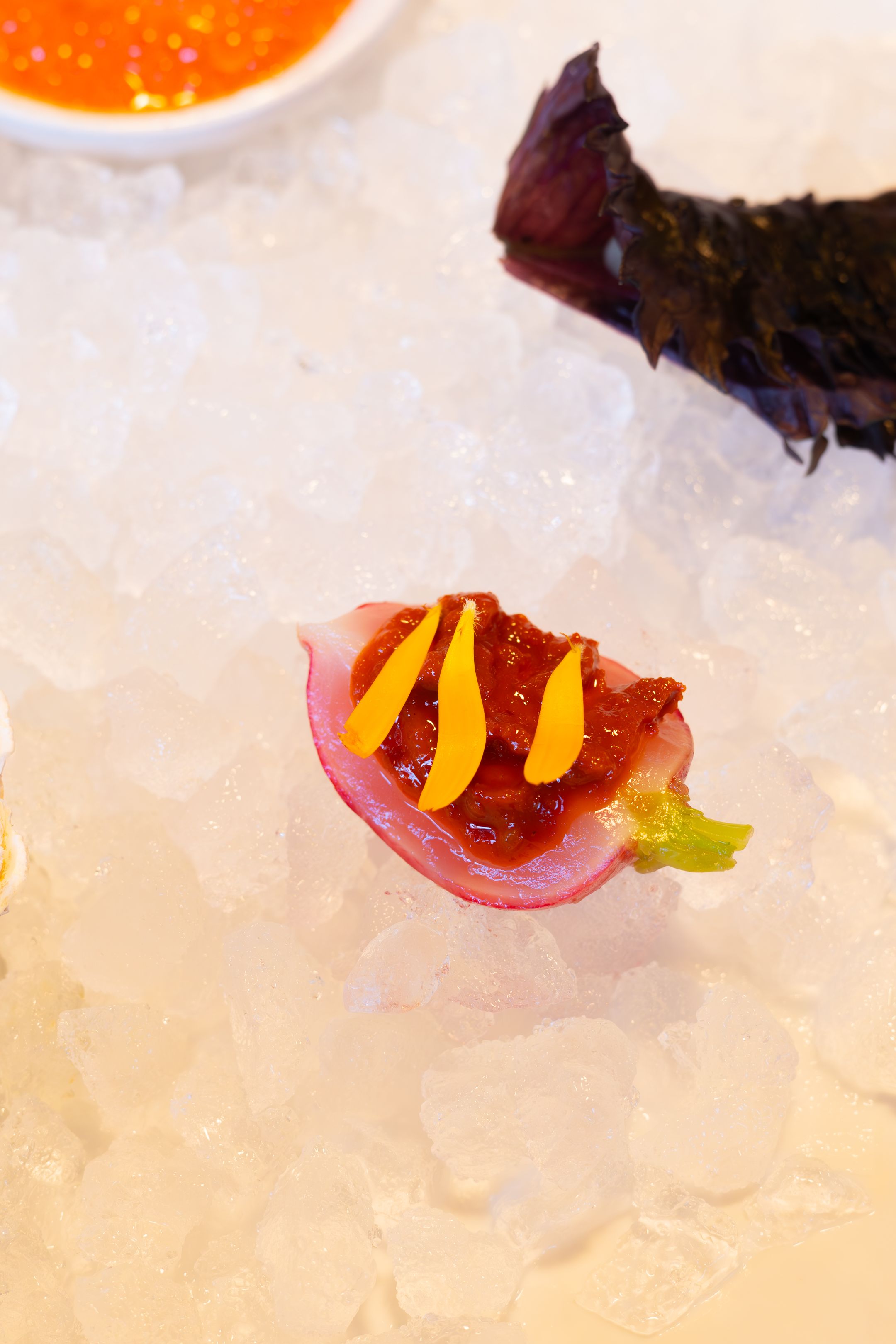 Colorful appetizer with yellow garnish served on pink base over ice.