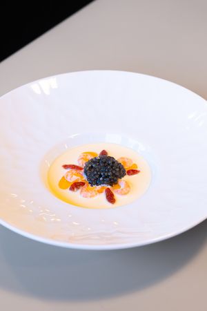 Elegant caviar dish with orange sauce and red garnish in white bowl.