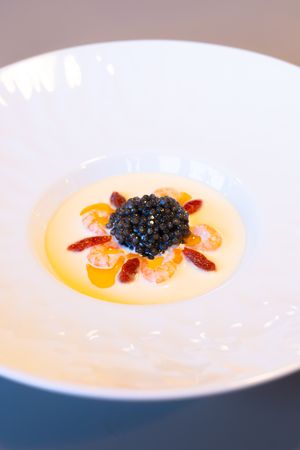Black caviar presented atop orange cream sauce with red garnish.